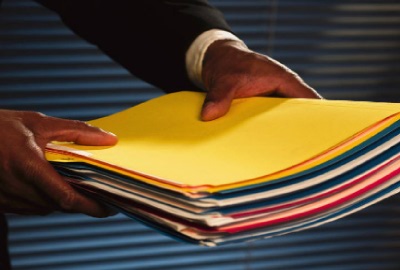 Image of man in a suit holding out a stack of file folders signifying that he intends to delegate the work.