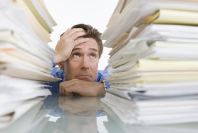 Image of distraught man behind a mountain of papers depicting the need to manage staff burnout.