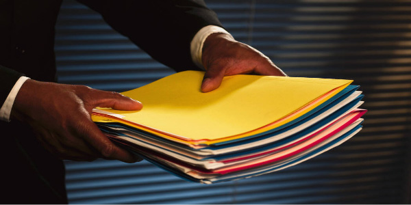 Image of man in a suit holding out a stack of file folders signifying that he intends to delegate the work.