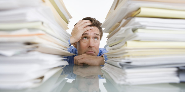 Image of distraught man behind a mountain of papers depicting the need to manage staff burnout.