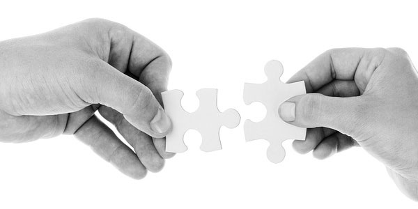 Image of two hands, each holding a puzzle piece signifying the need to employ project job descriptions.