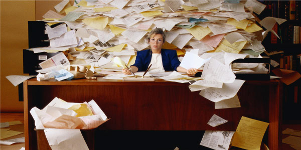 Image of woman at a desk in front of mountain of papers depicting the need to be ready for risky projects.